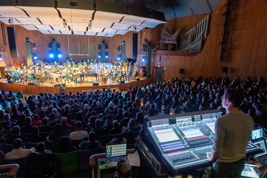 Soundboard operator behind a crowded audience watching and listening to a music ensemble from MIT in Kresge Auditorium.