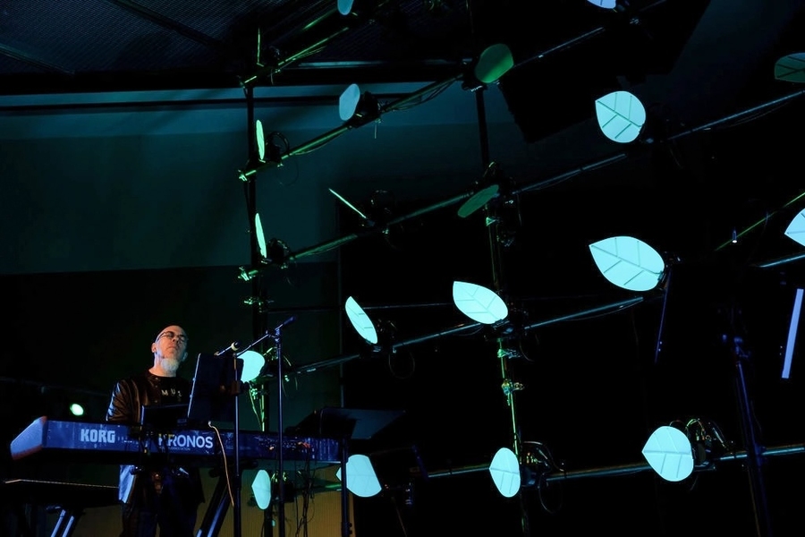 `Jordan Rudess performing on an electric keyboard next to a stage set with neon-lit leaves.