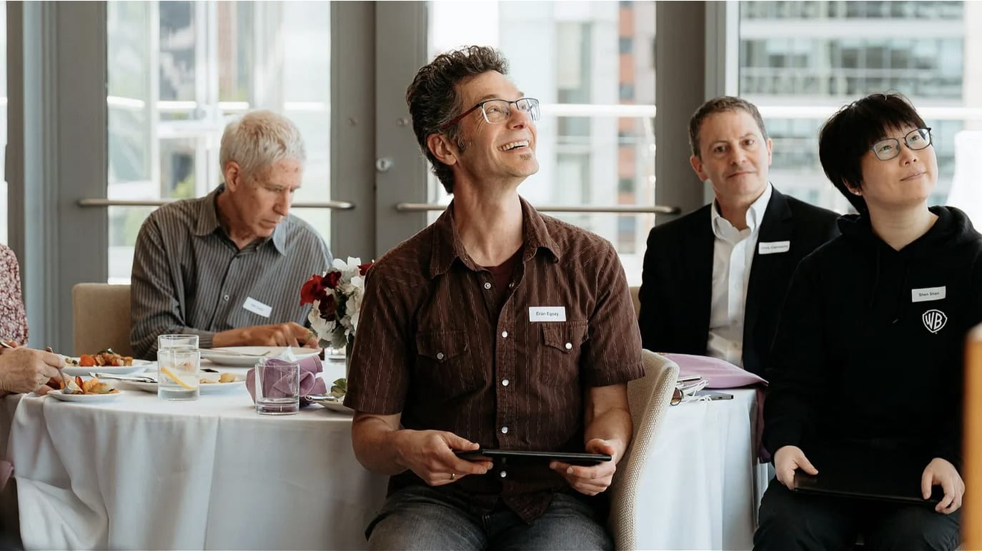 Eran Egozy seated at a full table of persons and smiling.